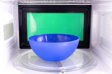 Young man heating food in the microwave. Green background for chroma key.
