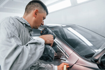 Applying new color. Caucasian automobile repairman in uniform works in garage