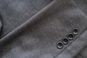High resolution with details and quality shot of formal black or dark grey wool suit fabric texture. with button decoration under light and shadow ambient. Ideal for background or wallpaper.