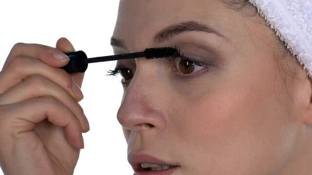 A young woman applies mascara on her lashes on a white background