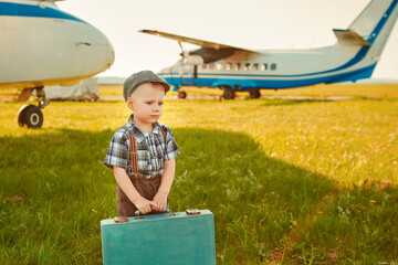 A cute little boy stands next to the propeller of an old airplane on a Sunny day.