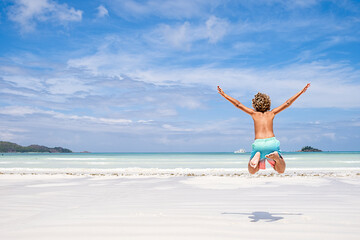 Young boy jumping of joy amd fun on tropical beach, summer holiday concept