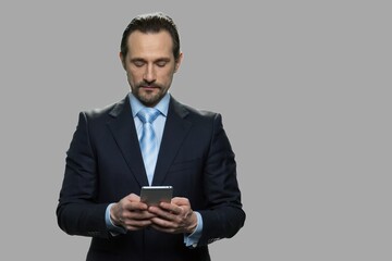 Attractive businessman using smartphone on gray background. Confident CEO using mobile phone. People, business and lifestyle concept.