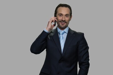 Smiling caucasian businessman talking on cell phone. Handsome male executive talks on mobile phone against gray background.