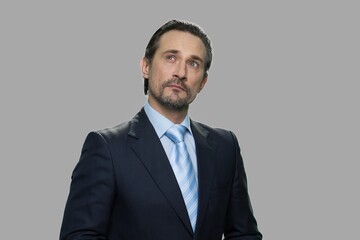 Portrait of confident businessman with thoughtful expression. Portrait of man in business suit looking pensive standing against gray background.