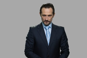 Agressive mature businessman looking at camera. Angry caucasian man in business suit against gray background. Negative facial expressions.