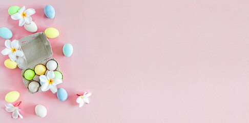 Fototapeta na wymiar Colorful Pastel Easter eggs with white frangipani flowers on pink background, top view with natural light. Flat lay style.