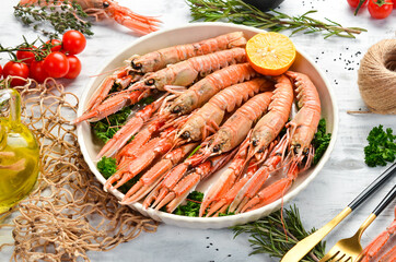 Boiled langoustines with parsley and spices on a plate. Norway lobster on a white wooden background. Top view. Free copy space.