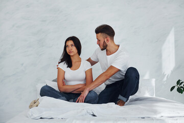 Offended young woman sits on the bed with her boyfriend at home