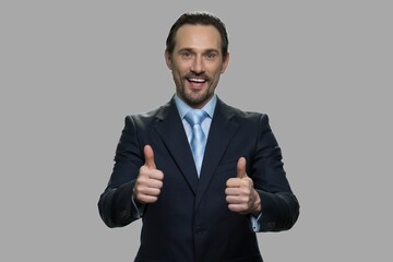 Successful businessman giving thumb up with both hands. Portrait of cheerful male executive on gray background.