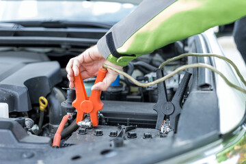 Hand putting pliers on the battery to start a car engine.
