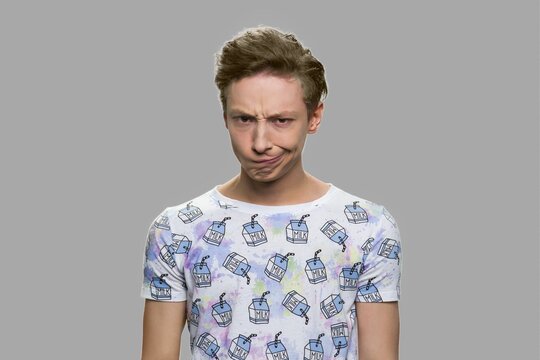 Teen boy making silly grimace. Funny teenage guy grimacing on gray background.
