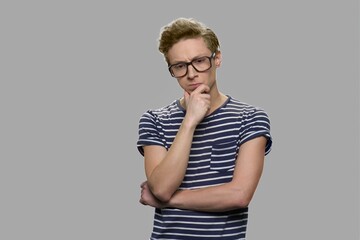 Thoughtful teenage boy wearing eyeglasses. Pensive teenage nerd boy wearing geek glasses on gray...