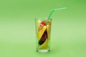 Slices of apple in glass with drinking straw on green background. Concept of fresh juice.