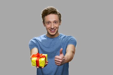 Teen boy showing gift box and thumb up. Cute caucasian guy giving gift box. Happy holiday concept.