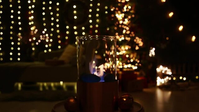 Selective focus on modern freestanding portable glass and copper metal fireplace burning bio ethanol gas on living room table with cozy Christmas eve home decor interior on background.