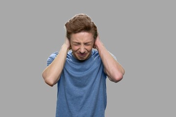 Teenage guy suffering from severe headache. Desperate teen boy on gray background close up.