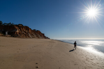 silhouette of a man jogging on an empty beach under the shining sun