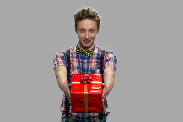 Portrait of teen boy offering gift box. Handsome caucasian guy giving present box against gray background.