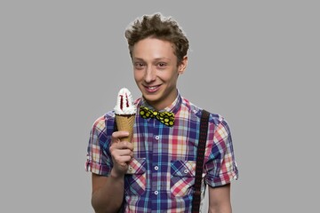 Cheerful teen boy holding cone ice cream. Portrait of handsome teenage guy with ice cream standing against gray background.