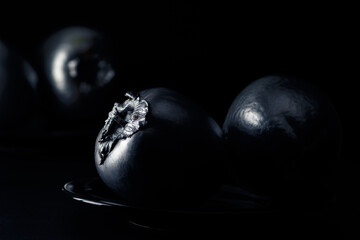 Artistic approach of natural and silver persimmons on a black background against light.