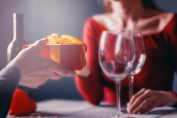 Congratulation concept for valentines day. couple at the table in a restaurant. dim lights, lovers give each other gifts.