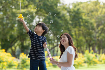 Asian family having fun mother and her son playing with soap bubbles in the park together