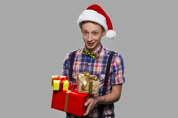 Teen boy in Santa Claus hat holding gift boxes. Portrait of teenage guy holding Christmas gifts on gray background.