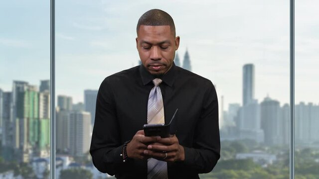 African America man texting on phone in office while camera pans right. View of city background