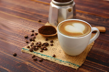 hot latte coffee in white ceramic cup  with roasted coffee beans  ground coffee on wood spoon on brown sack