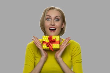 Amazed woman with gift box looking at camera. Shocked woman holding present box on gray background. What a surprise.