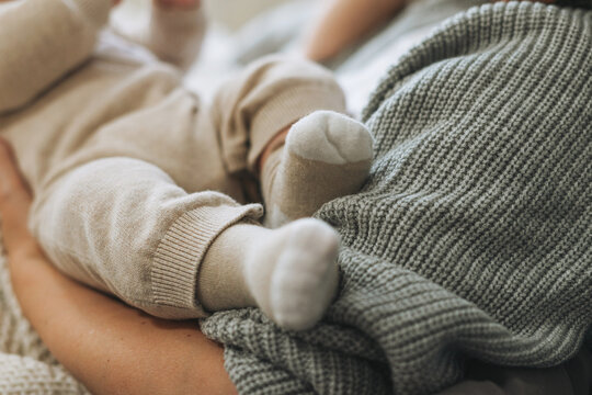 Cute baby feet in beige socks, child with mother on the bed, happy motherhood