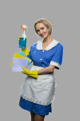 Attractive maid woman holding cleaner spray. Full length portrait of smiling cleaning woman showing rags and bottle of detergent.