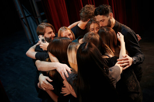 Embracing each other. Group of actors in dark colored clothes on rehearsal in the theater
