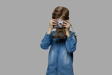 Little boy using old retro camera. Cute child in denim jacket taking picture with aged photo camera against gray background. Young handsome photographer.