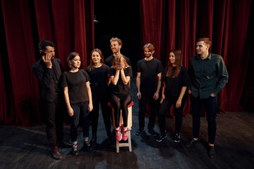 Girls sits on chair and crying. Group of actors in dark colored clothes on rehearsal in the theater