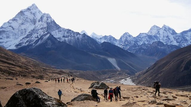 Large group of trekkers and porters on the exhausting way to Lobuche at high altitute on Everest Base Camp Trek in Khumbu region, Nepal in the Himalayas with majestic snow-capped mountain Ama Dablam.