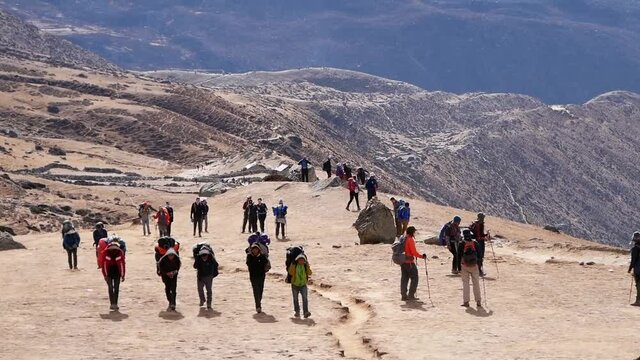 Large group of trekkers and porters with backpacks on Everest Base Camp Trek between Dingboche and Lobuche, Khumbu, Nepal in the Himalayas with sparse and rocky landscape.
