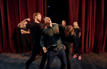 Fight scene. Group of actors in dark colored clothes on rehearsal in the theater