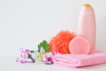 Obraz na płótnie Canvas Pink shampoo bottle, soap, towel and orange wisp. Colorful flowers. Simple female products for body washing. Closeup. Front view. Empty place for text or logo on light gray wall background.