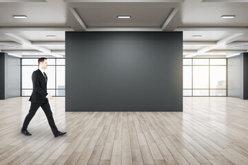 Fototapeta na wymiar Businessman walking in gallery interior with empty black wal