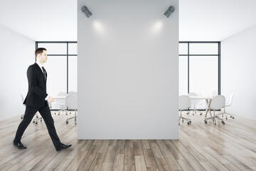 Businessman walking in in conference room with blank white wall.