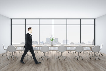 Businessman walking in conference room with meeting table and city view.
