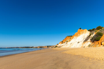 Fototapeta na wymiar panorama view of a wide empty golden sand beach with colorful sand cliffs on a sunny day