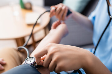 cropped view of nurse measuring blood pressure of patient with tonometer, blurred background