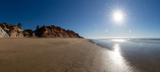 panorama view of a wide empty golden sand beach with colorful sand cliffs on a sunny day