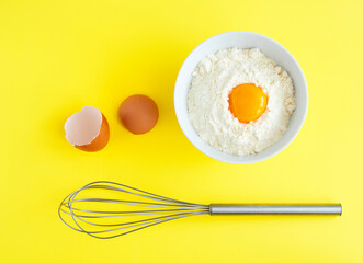 Flat lay composition. Ingredients for baking egg, flour, whisk on a yellow background. 