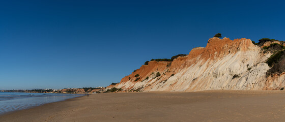 panorama view of a wide empty golden sand beach with colorful sand cliffs on a sunny day