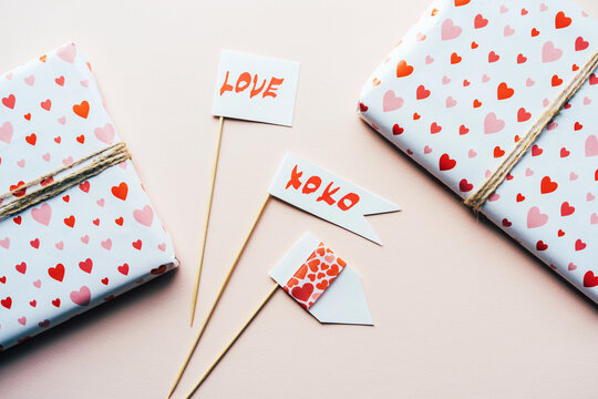Valentine's holiday flags. Valentine's day background. Gifts in wrapping paper with pattern hearts, props on pastel pink background.