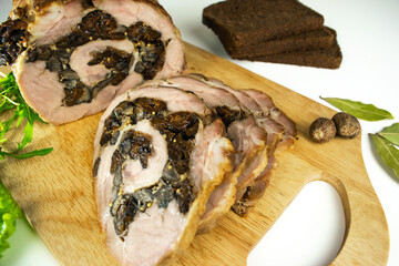 Baked meatloaf pork with prunes and mushrooms cut into pieces on a cutting board.